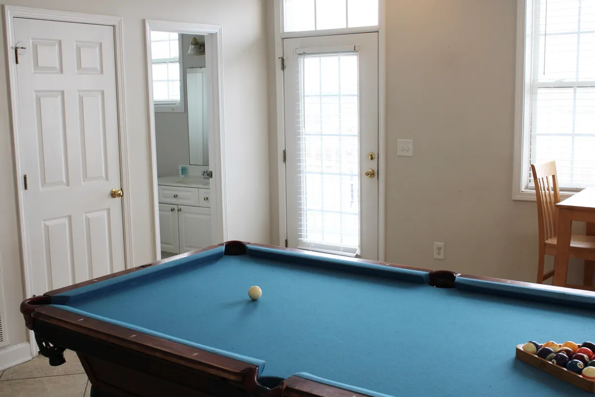 An open, casual recreation space with a pool table and dining table, doors leading outside, and a welcoming, light-filled ambiance. The setup invites guests to engage in pool games, socialize, or celebrate special occasions, reinforcing the room's versatility for entertainment.
