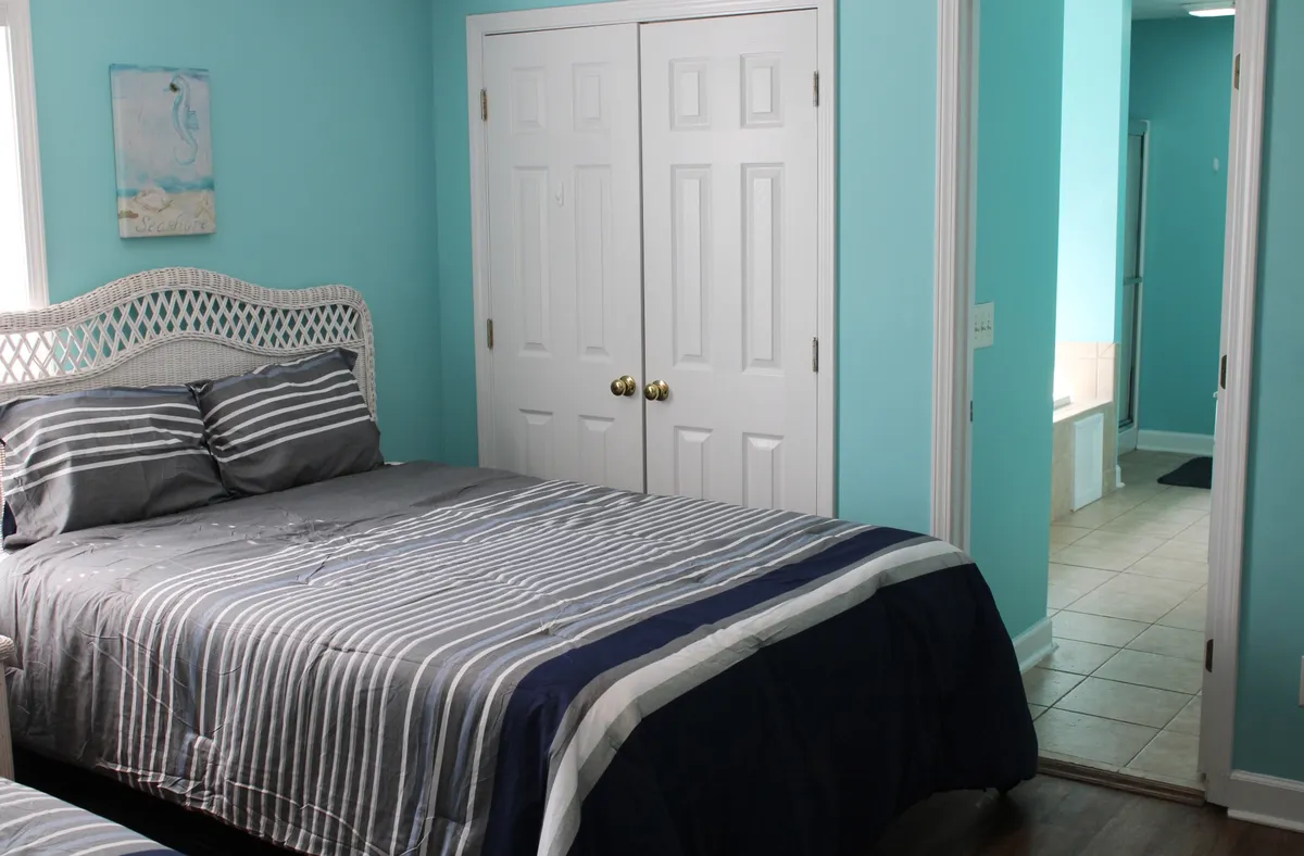 A single bed with striped bedding and a woven headboard takes center stage in this calm, blue-walled room. The scene is softened by closet doors and gentle lighting, evoking a sense of peaceful solitude ideal for restful sleep.