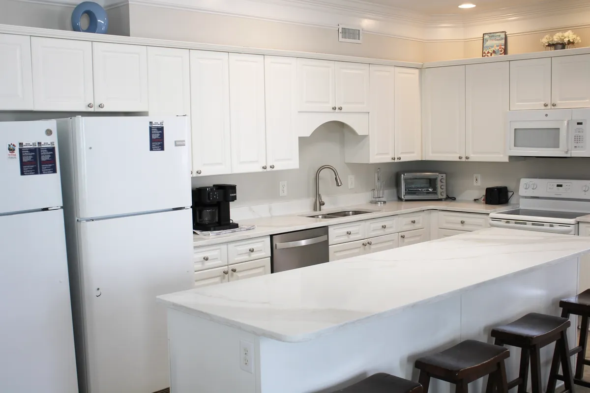 A welcoming kitchen with white cabinetry, a spacious kitchen island with bar stools, stainless steel appliances, and plenty of room for group meal preparation and entertaining. The island invites guests to gather for casual breakfasts or help with cooking.