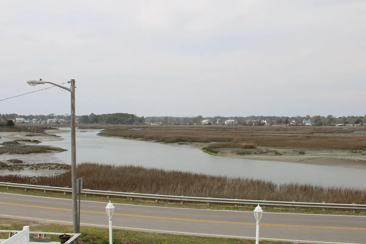 A wide view of marshland and a river with distant houses and a road, inviting guests to explore the natural beauty beyond the villa. The peaceful landscape highlights opportunities for walks, birdwatching, and discovering the local area.