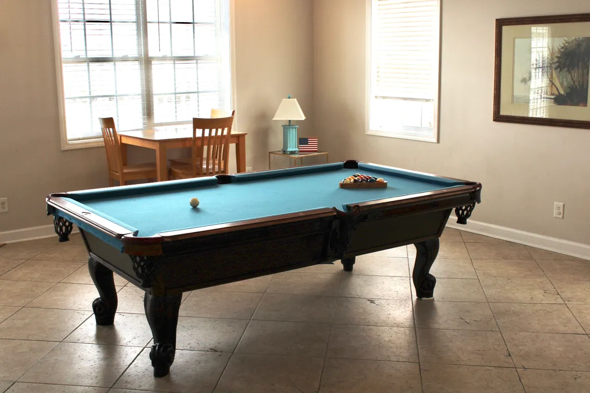 A spacious recreation room featuring a modern pool table and a dining table set beneath soft lighting. The scene conveys a relaxed atmosphere perfect for socializing, playing games, or sharing casual meals. The layout encourages group activities and friendly competition.