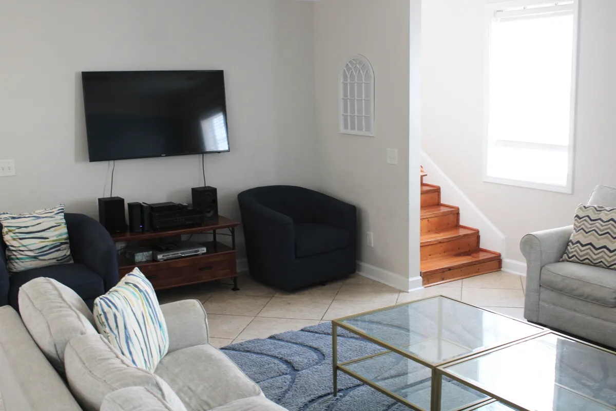 A cozy living area furnished with a comfortable sofa, glass coffee table, wooden staircase, and a wall-mounted television. The space is set up for relaxing, watching TV, or enjoying movie nights, echoing the villa's promise of memorable evenings spent together.