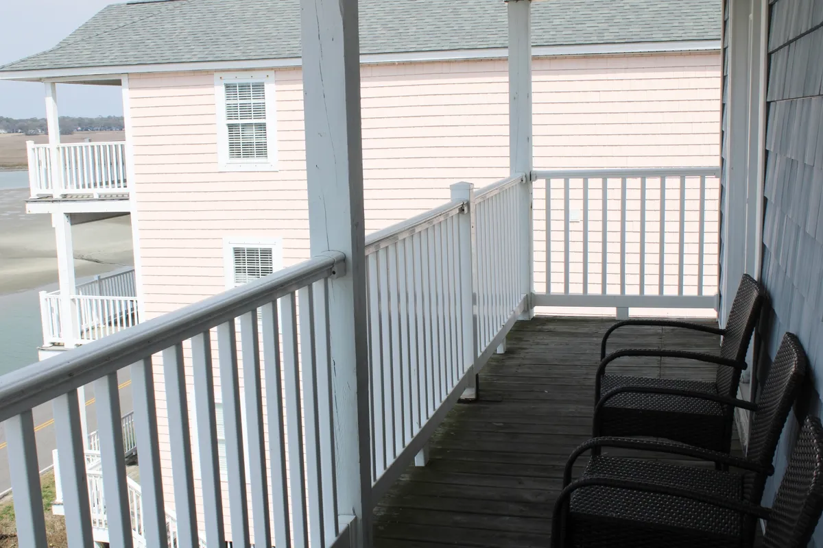 A private balcony with a sturdy railing overlooks a mix of natural and residential scenery. There is a cozy seating area, perfect for relaxing while taking in the view. The space feels inviting and is positioned to maximize enjoyment of the outdoors, whether for sunrise or stargazing.